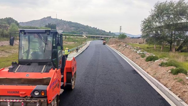 6月18日，由球王会平台承建的东乡县那勒寺镇沿川经济带产业道路施工现场机械轰鸣，沥青摊铺机缓缓向前推进，滚烫的沥青混合料均匀摊铺在水稳层上，压路机紧随其后反复碾压，一条黝黑发亮的“黑色丝带”向远